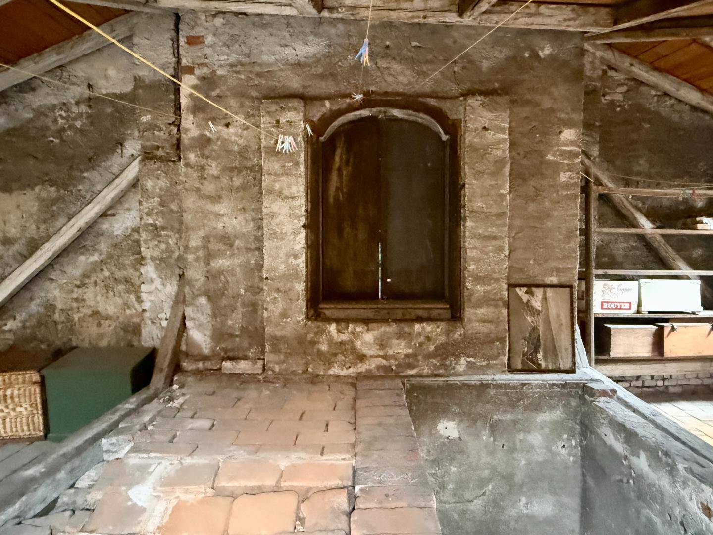 Rustikaler Dachboden mit unverputzten Ziegelwänden, Holzbalken und einem kleinen Fenster.