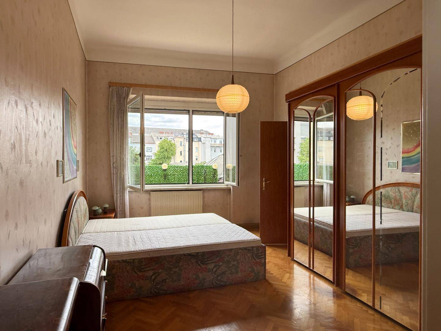 Schlafzimmer mit Doppelbett, Spiegelschrank und Fenster mit Blick ins Grüne.