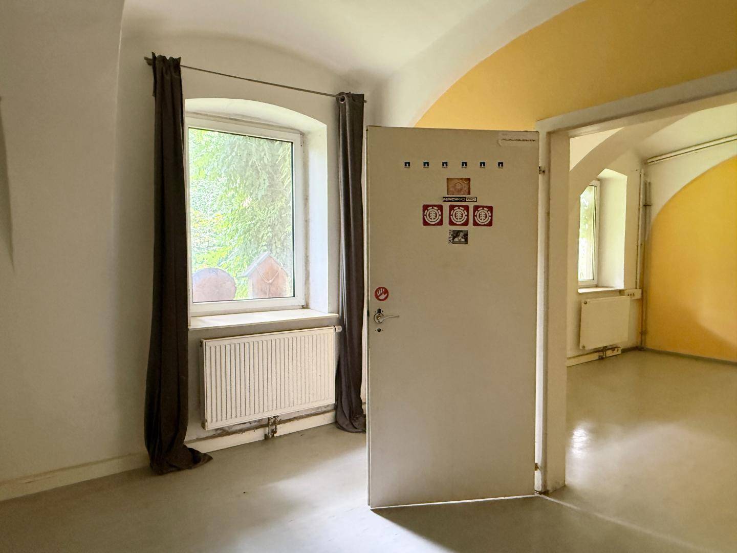 Heller Raum mit weiß gestrichenen Wänden, gelbem Bogen und Fenster mit Blick ins Grüne.