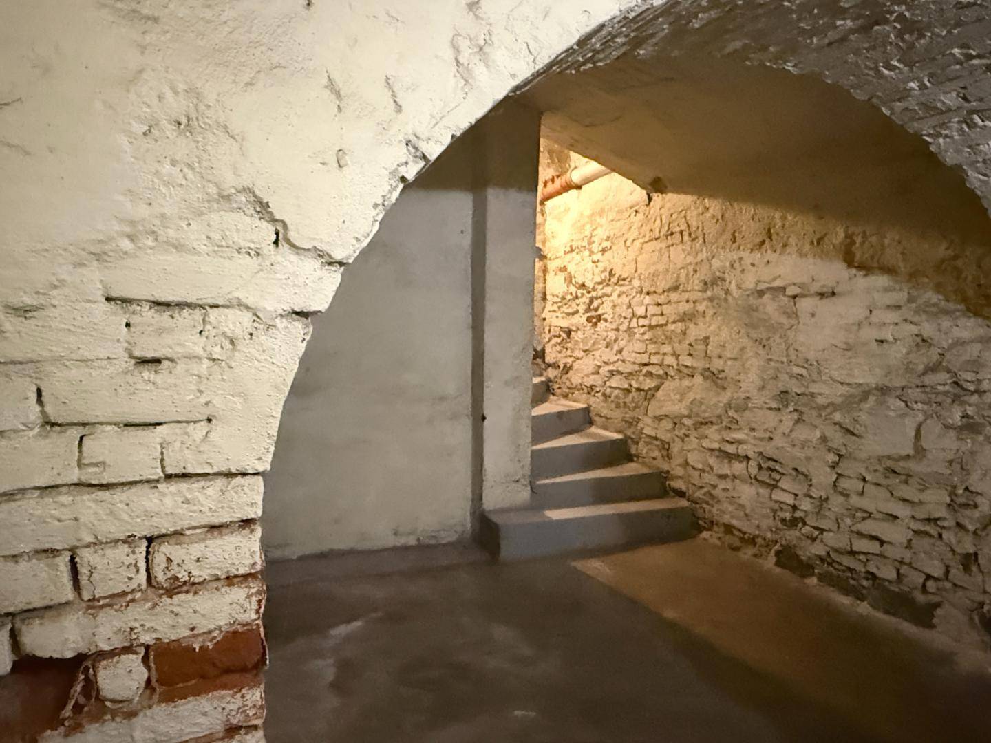 Kellerraum mit gewölbten Ziegeldecken und einer Steintreppe, die in einen weiteren Bereich führt.