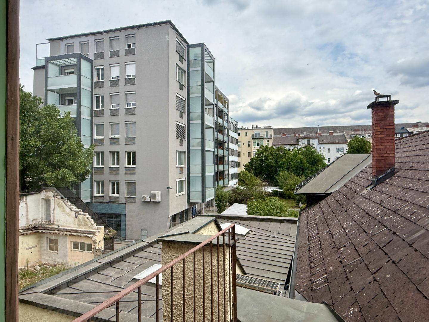 Weitblick über Dächer und moderne Gebäude der Stadt, mit einem Schornstein im Vordergrund.