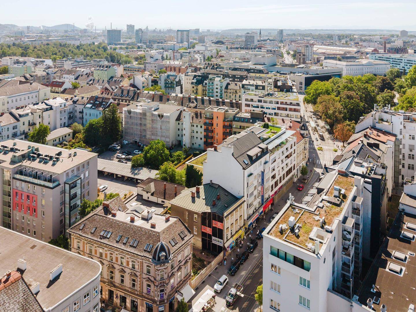 Luftaufnahme einer städtischen Umgebung mit dicht bebauten Straßen, verschiedenen Gebäudetypen und Grünflächen.