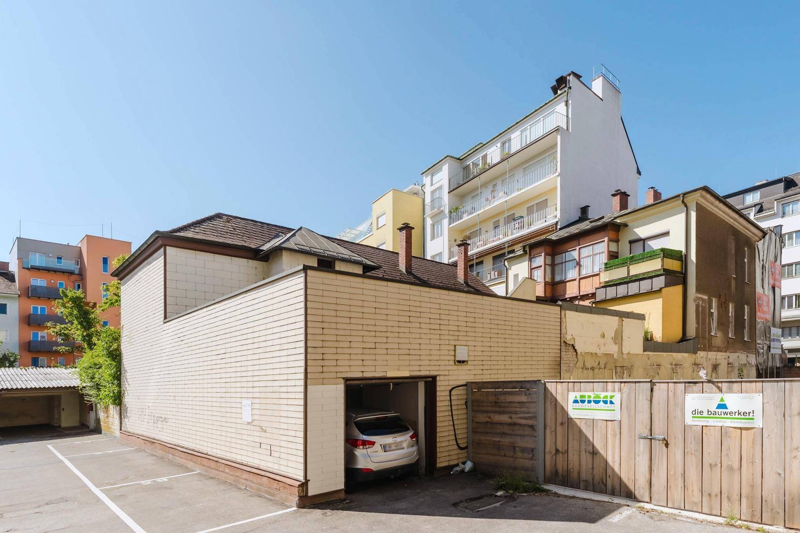 Rückansicht eines älteren Gebäudes mit einer Garage und mehreren Parkplätzen im Freien.