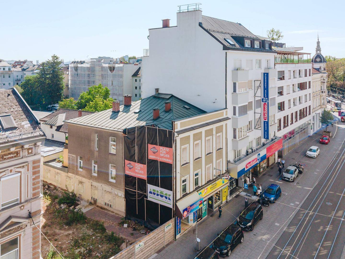 Luftaufnahme einer Stadtstraße mit Gebäuden, von denen einige renoviert werden, und Straßenbahnschienen.