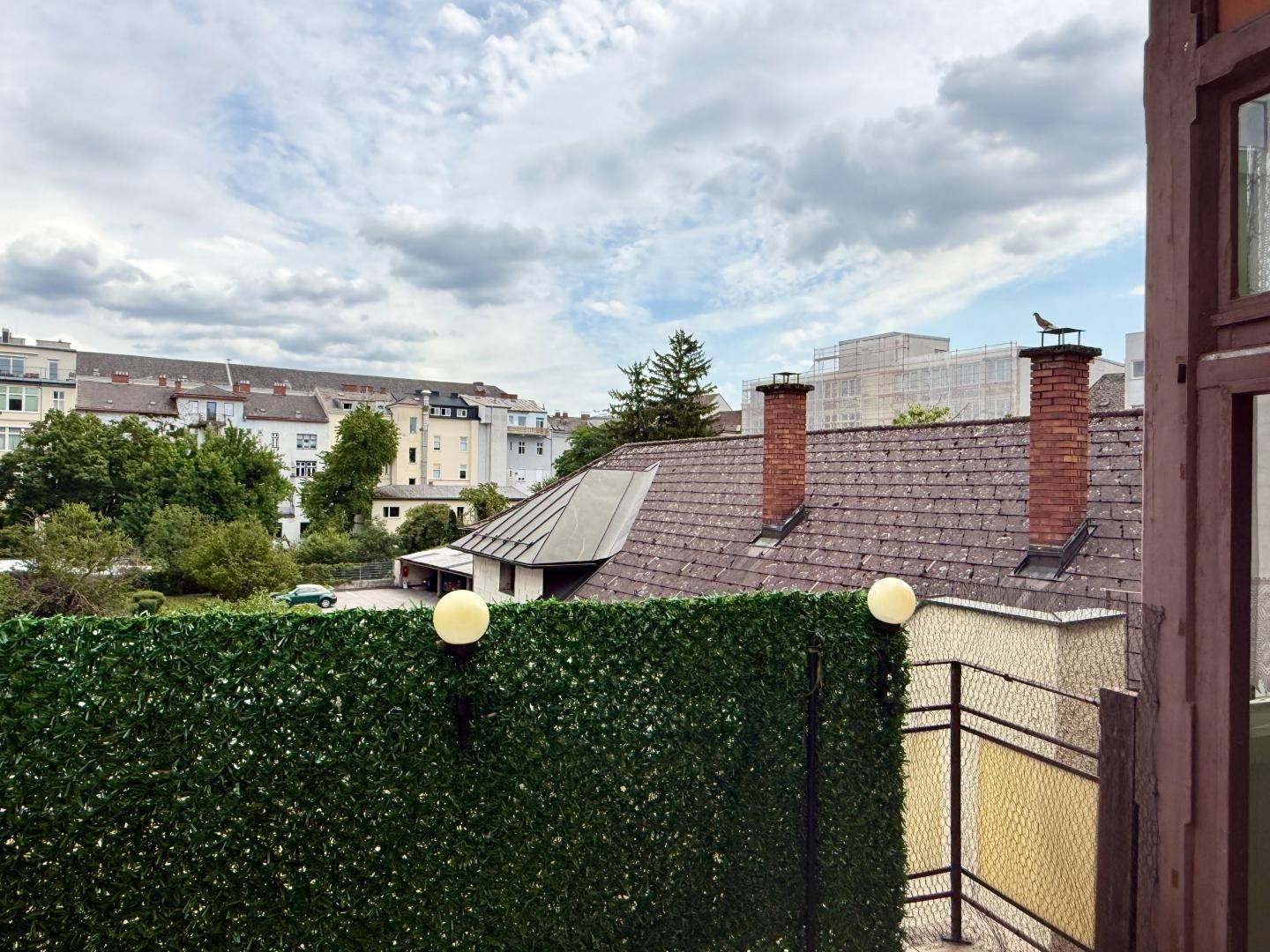 Blick über Dächer und Schornsteine auf die umliegende Stadtlandschaft mit Bäumen und Gebäuden.