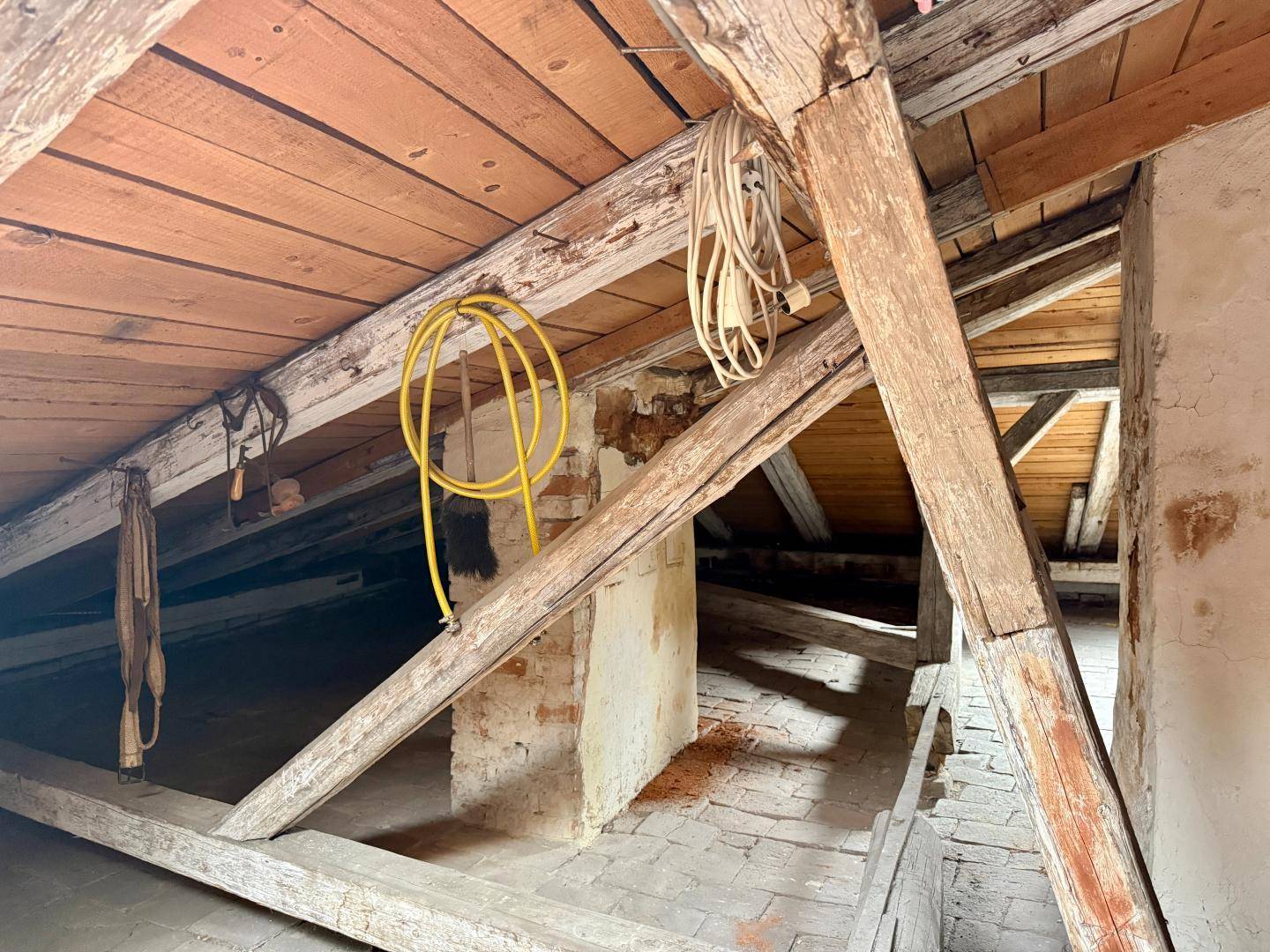 Dachboden mit sichtbaren Holzbalken, losem Kabel und einer rohen, unfertigen Ästhetik.