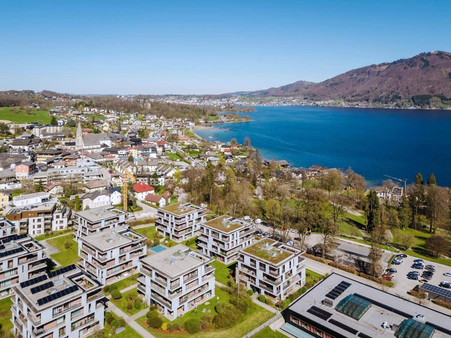 Überblick über die moderne Wohnanlage am Seeufer mit umliegender Stadt und Berglandschaft.