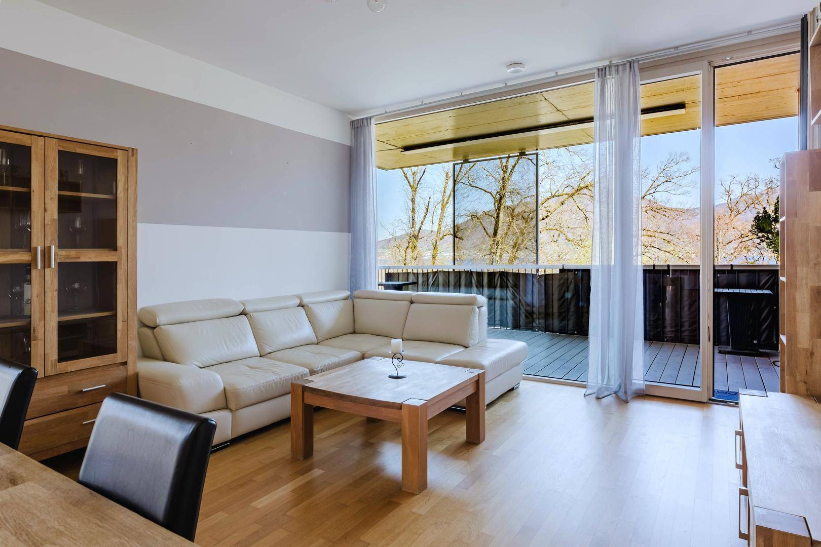 Gemütliches Wohnzimmer mit heller Ledercouch, Holztisch und großem Balkon mit Ausblick.