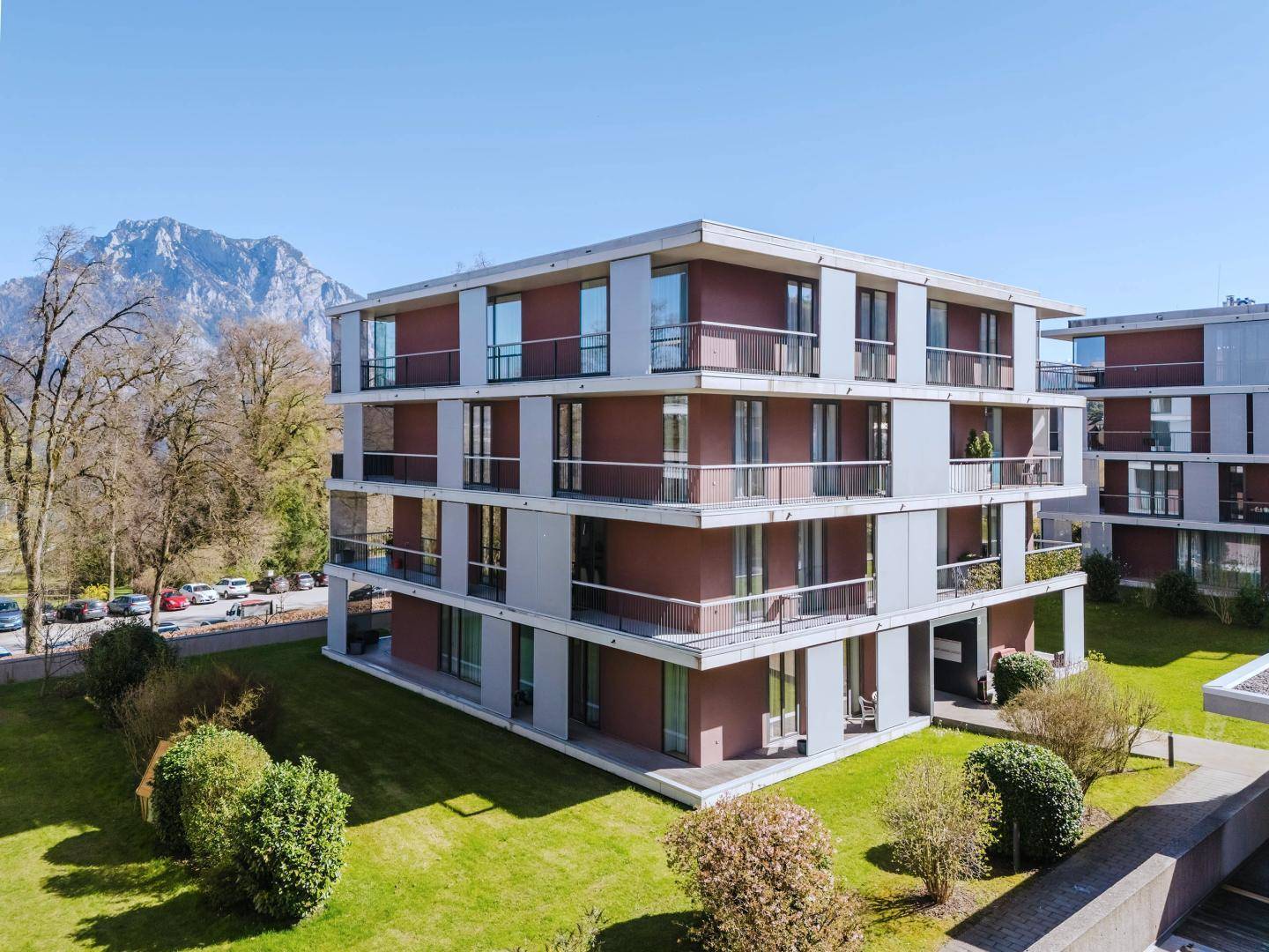 Modernes Wohngebäude mit klarer Architektur, großen Glasflächen und umliegenden Grünanlagen.