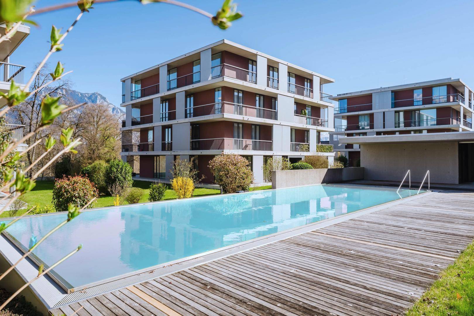 Modernes Wohngebäude neben einem eleganten Außenpool mit Holzdeck und Bergblick.