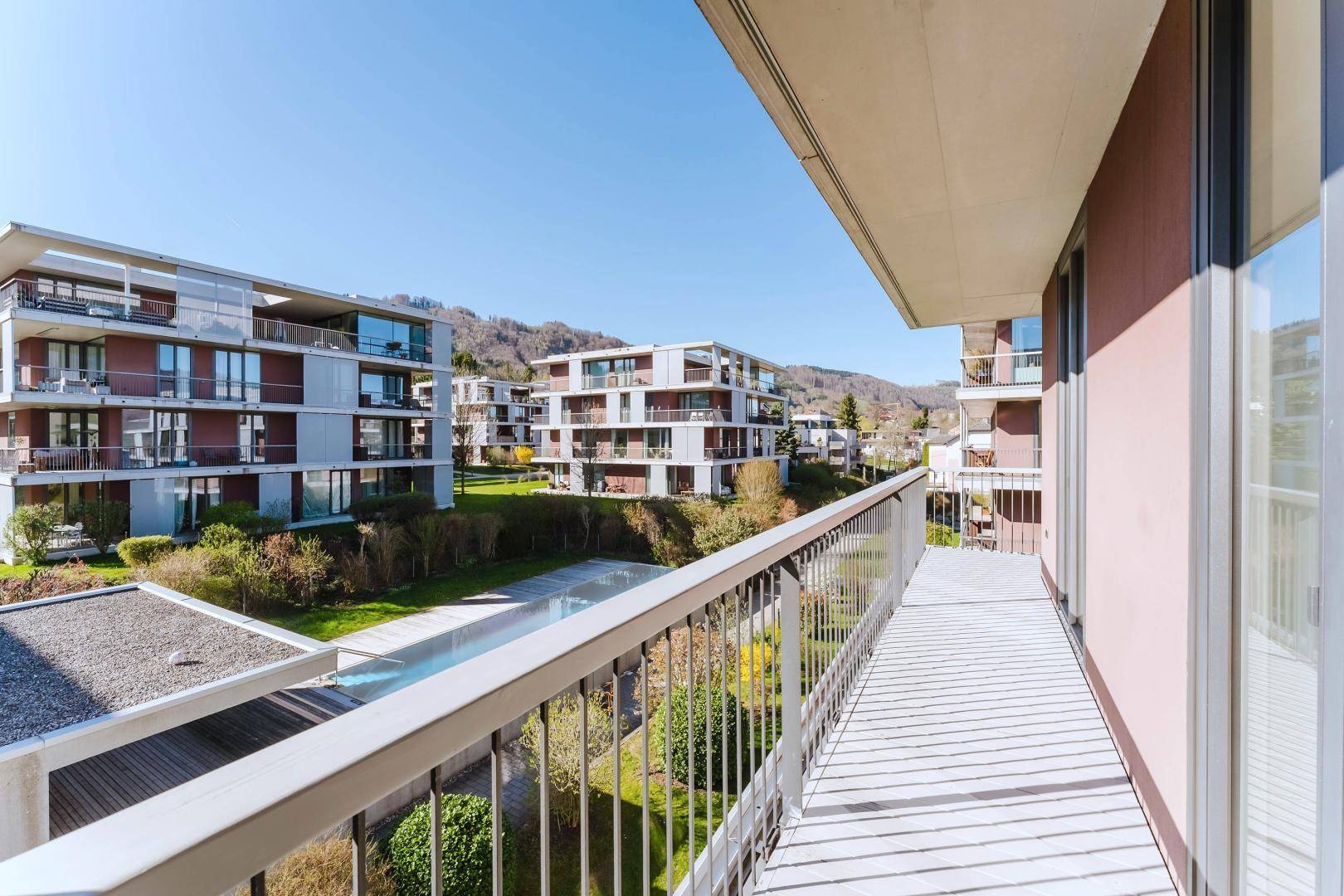 Langer Balkon mit Metallgeländer und Blick auf die umliegenden Gebäude und Grünflächen.
