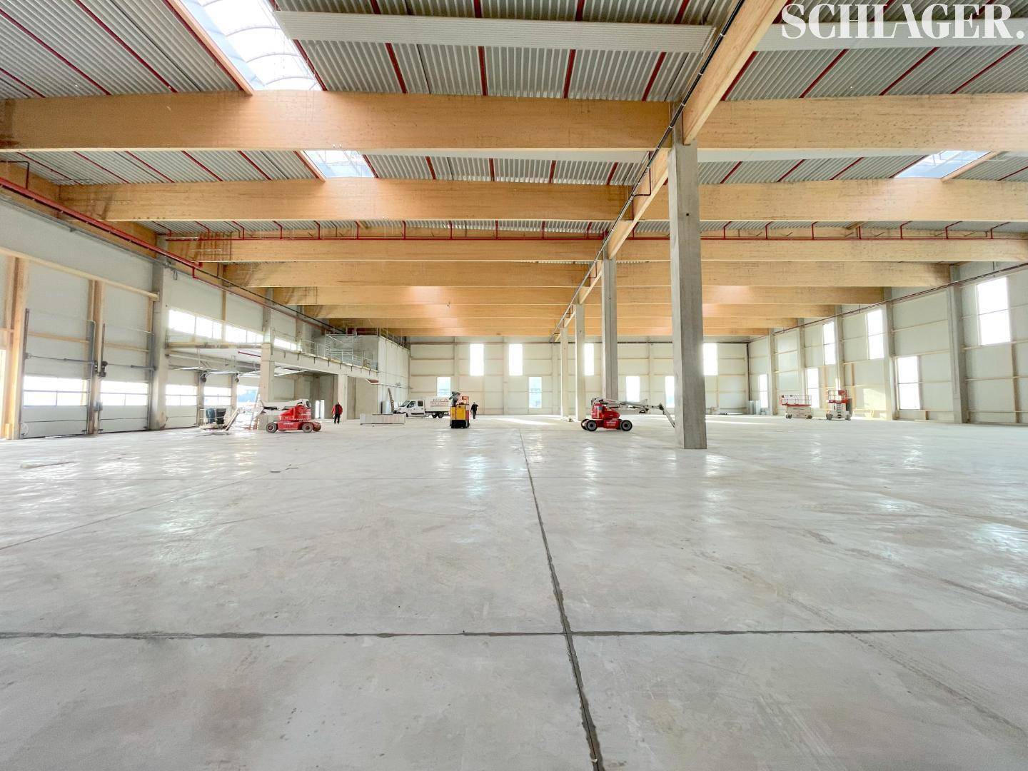 Geräumige, leere Lagerhalle mit hohen Decken, sichtbaren Holzträgern und viel Tageslicht durch Oberlichter.