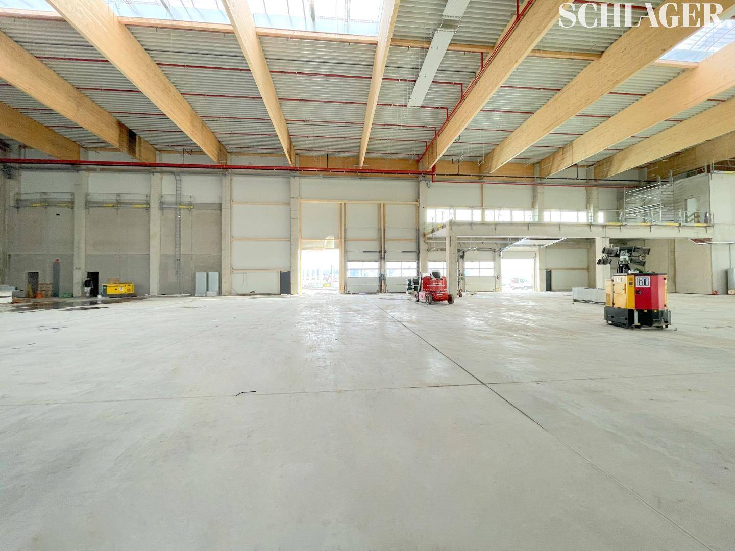Weitläufige Industriehalle mit hohen Decken, Holzbalken und großen Toren, die viel natürliches Licht hereinlassen.