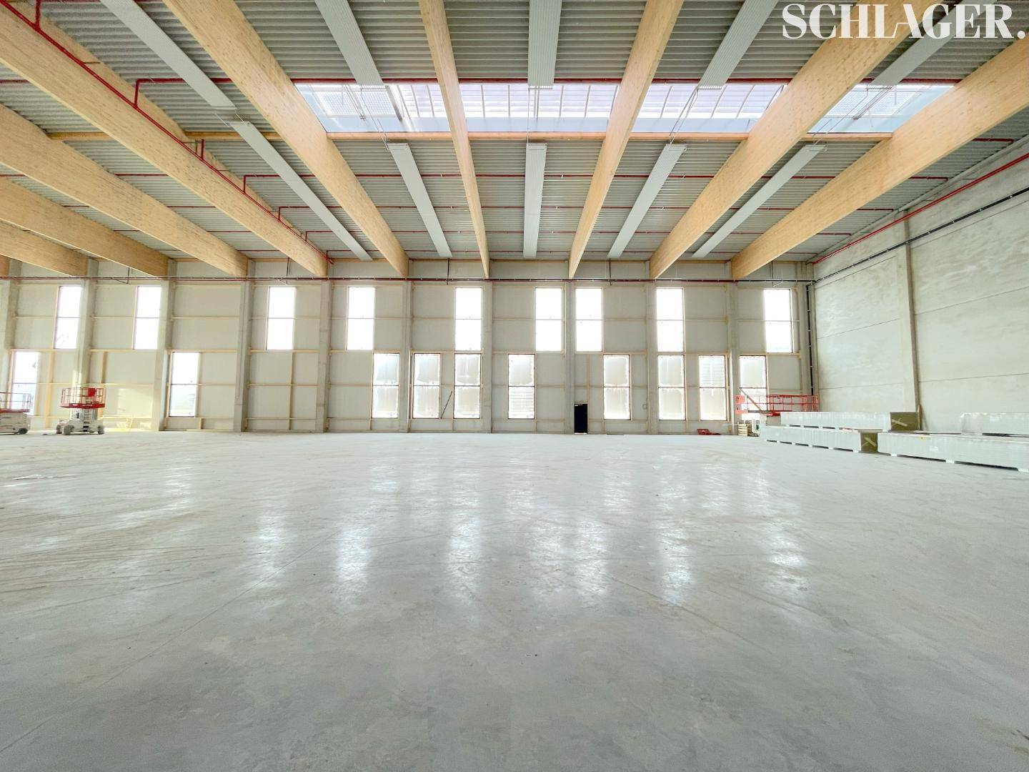Große, leere Industriehalle mit hohen Decken, Holzkonstruktion und vielen Fenstern, die für eine helle Atmosphäre sorgen.