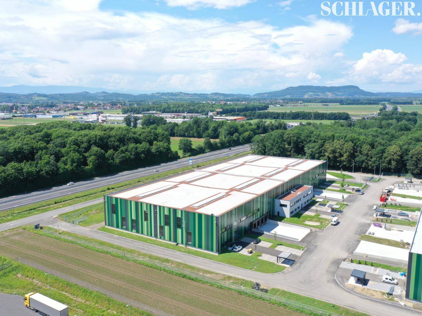 Luftaufnahme eines einzelnen modernen Industriegebäudes mit Parkplätzen und einer Autobahn in der Ferne.