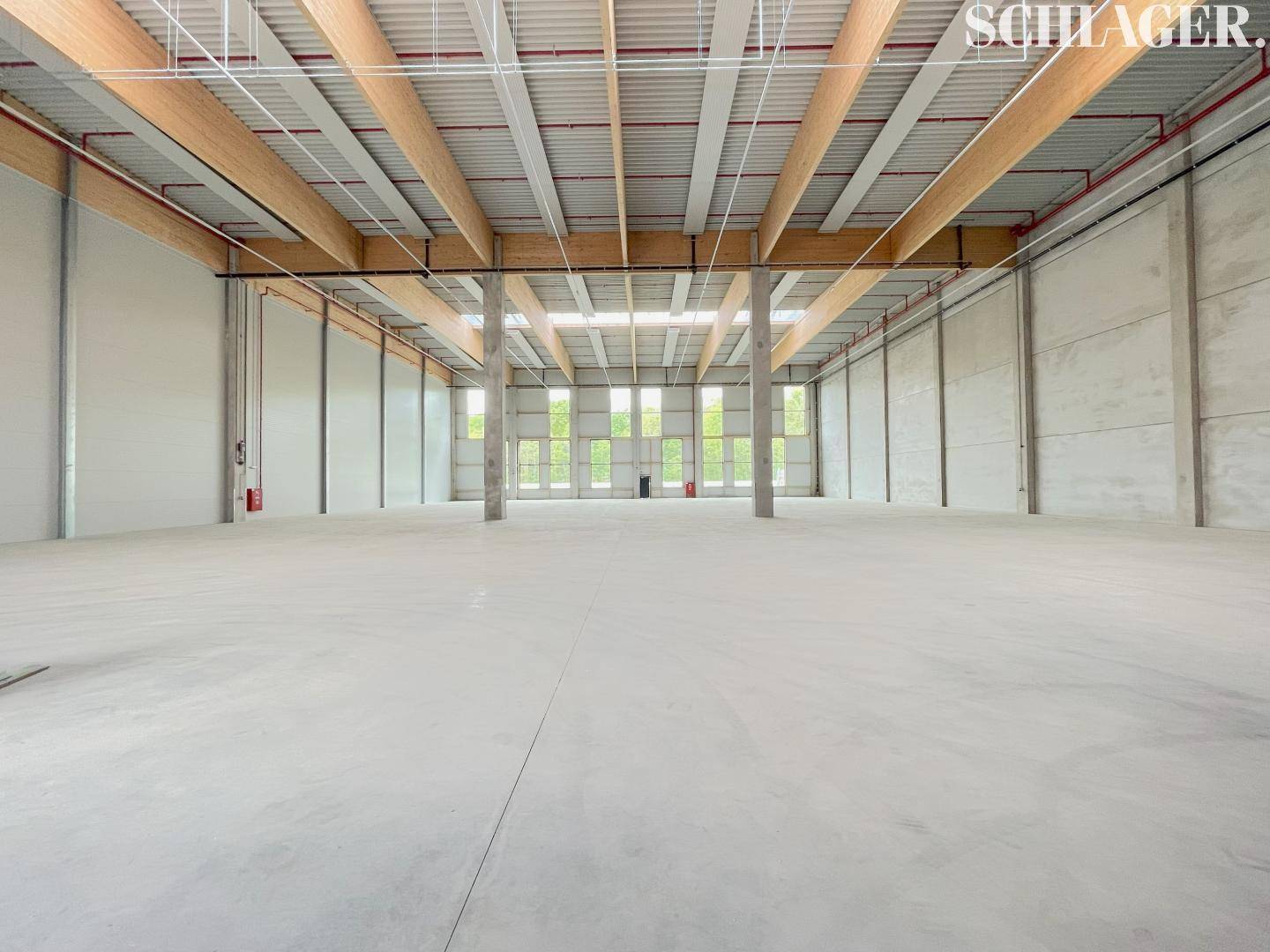 Geräumige, leere Lagerhalle mit hohen Decken, sichtbaren Holzbalken und einem polierten Betonboden.