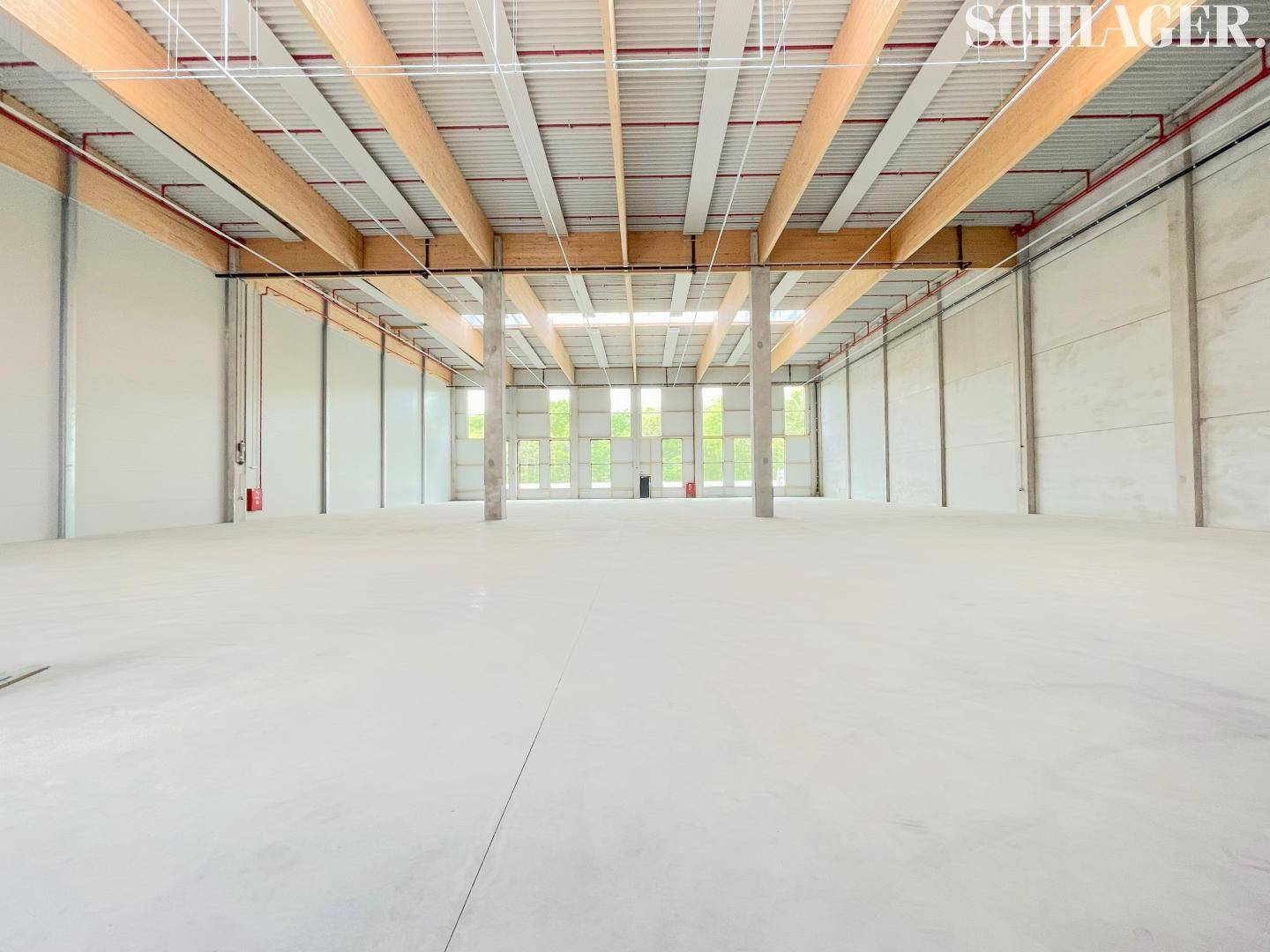 Weitläufiger Innenraum einer Lagerhalle mit hohen Decken, sichtbaren Holzbalken und einem hellen Betonboden.