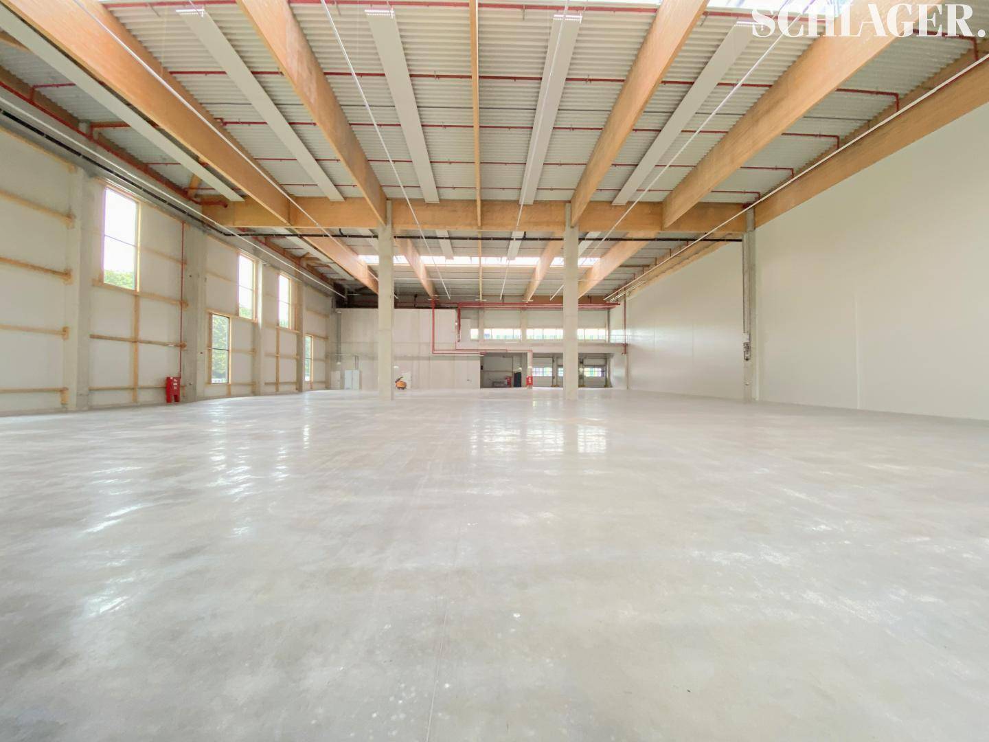 Große, unmöblierte Lagerhalle mit hohen Decken, Holzbalkenkonstruktion und großen Fenstern für viel Tageslicht.