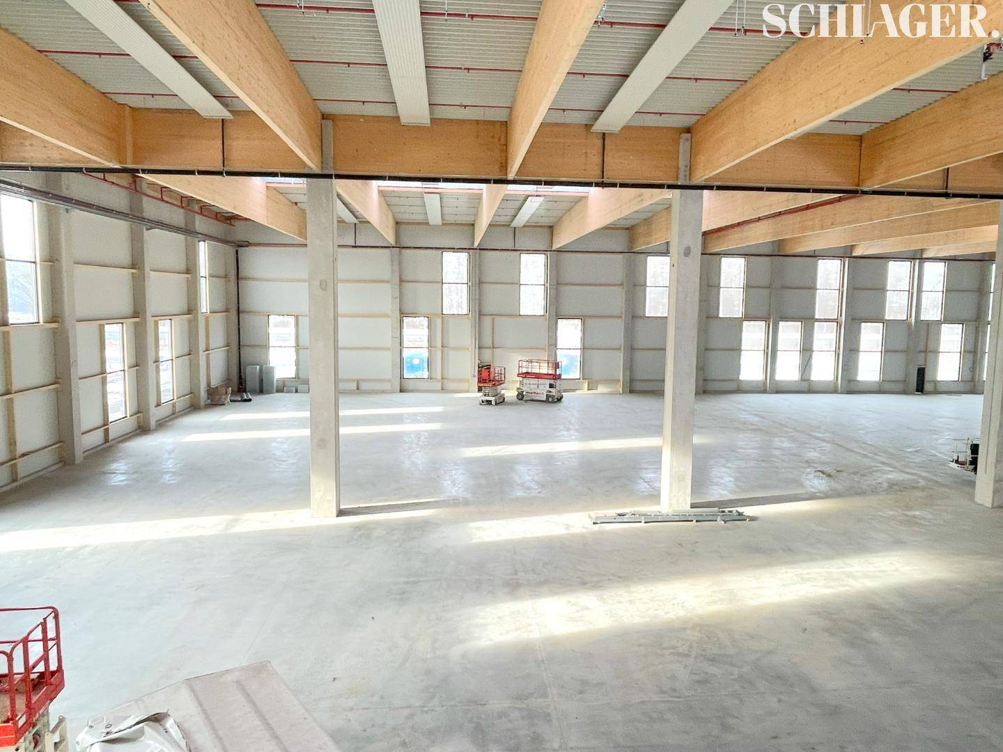 Helle, leere Industriehalle mit hohen Decken, Holzbalken und zahlreichen Fenstern für optimale Tageslichtnutzung.