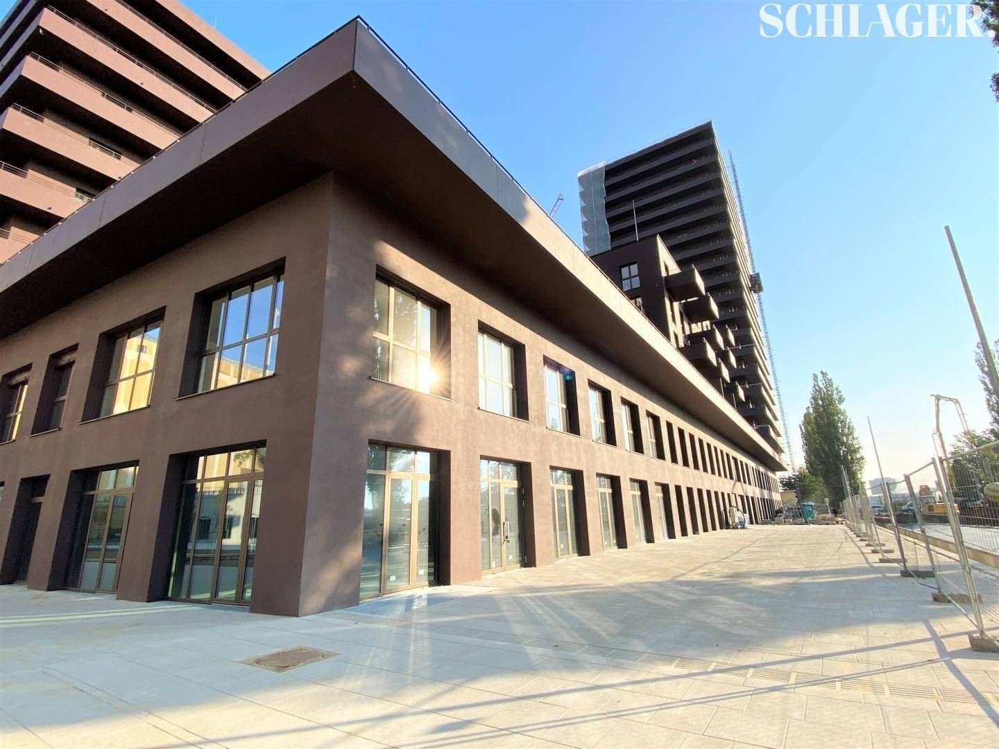 Erdgeschossfassade eines modernen Gebäudes mit großen Fensterfronten und braunem Putz an einem sonnigen Tag.