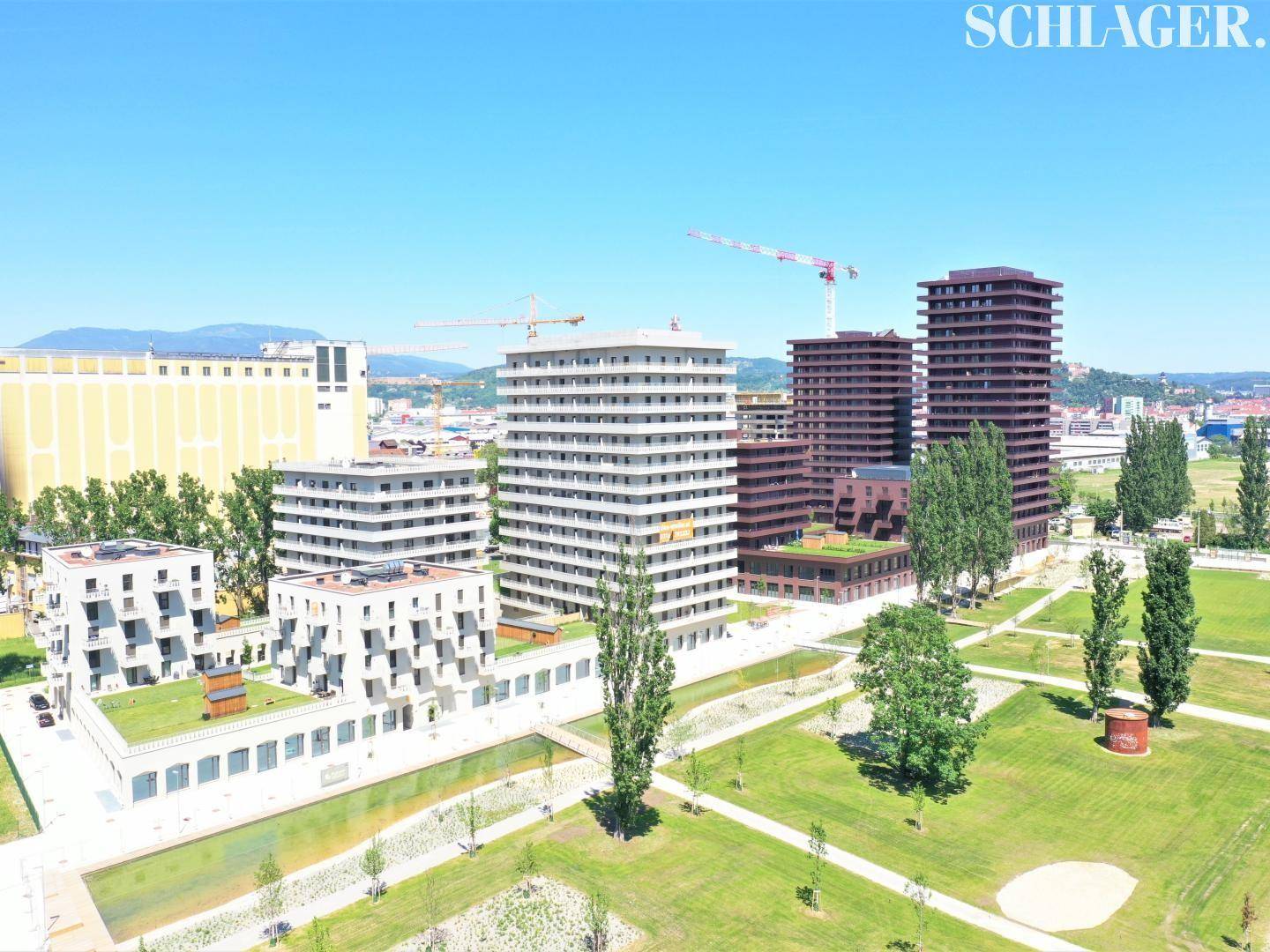 Luftaufnahme eines modernen Wohnkomplexes mit mehreren Gebäuden, Grünflächen und einem Wasserlauf.
