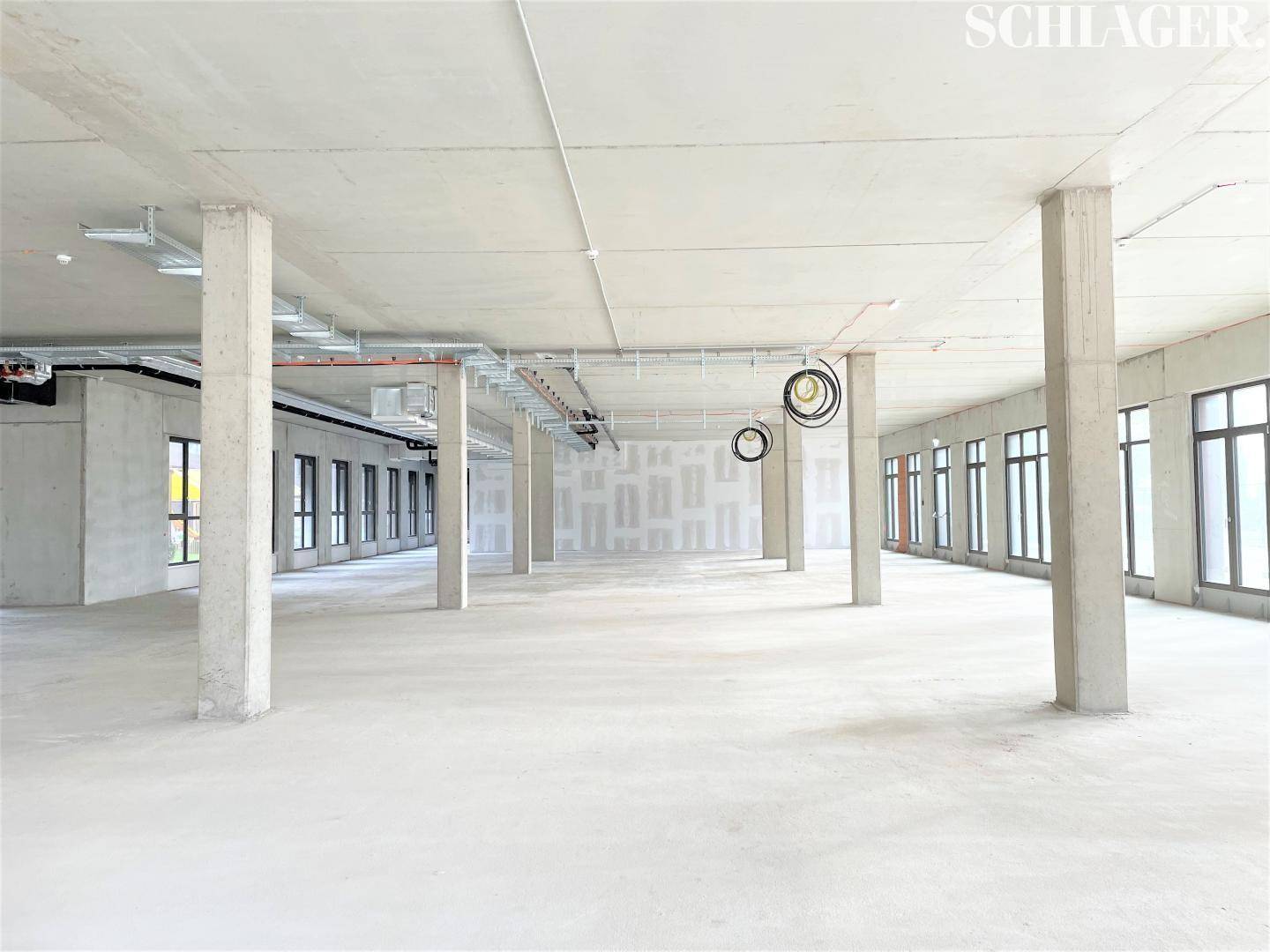 Heller, weitläufiger Gewerberaum mit Betonstützen, großen Fenstern und sichtbaren Deckeninstallationen.