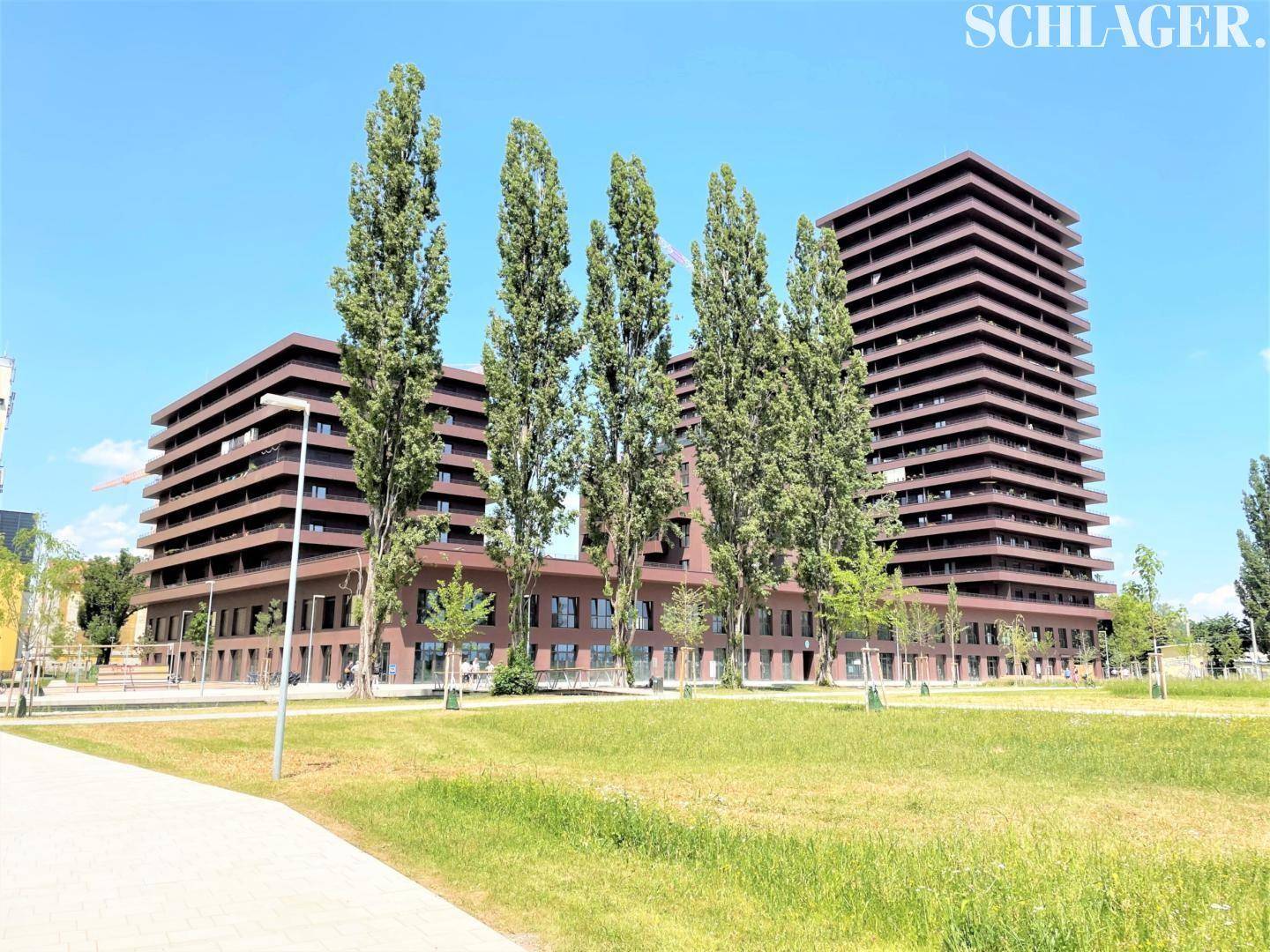 Großer moderner Gebäudekomplex mit brauner Fassade und vielen Fenstern, umgeben von einer weitläufigen Grünfläche.