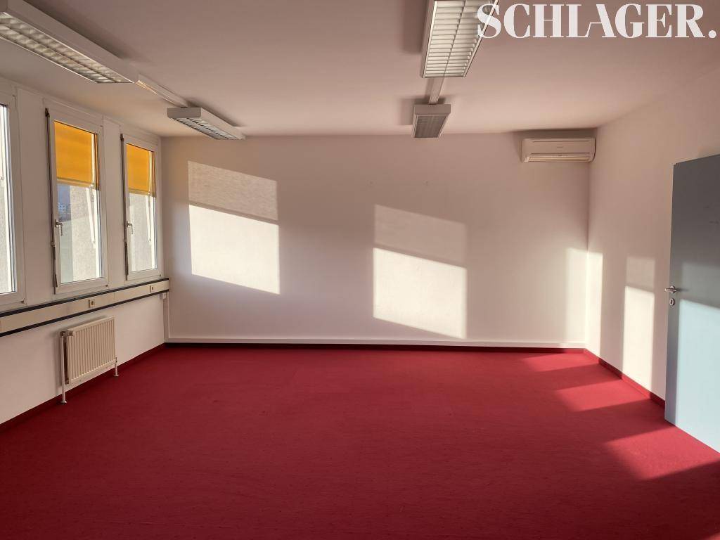 Helles Büro mit rotem Teppichboden, Klimaanlage und großen Fenstern, ideal für gewerbliche Nutzung.