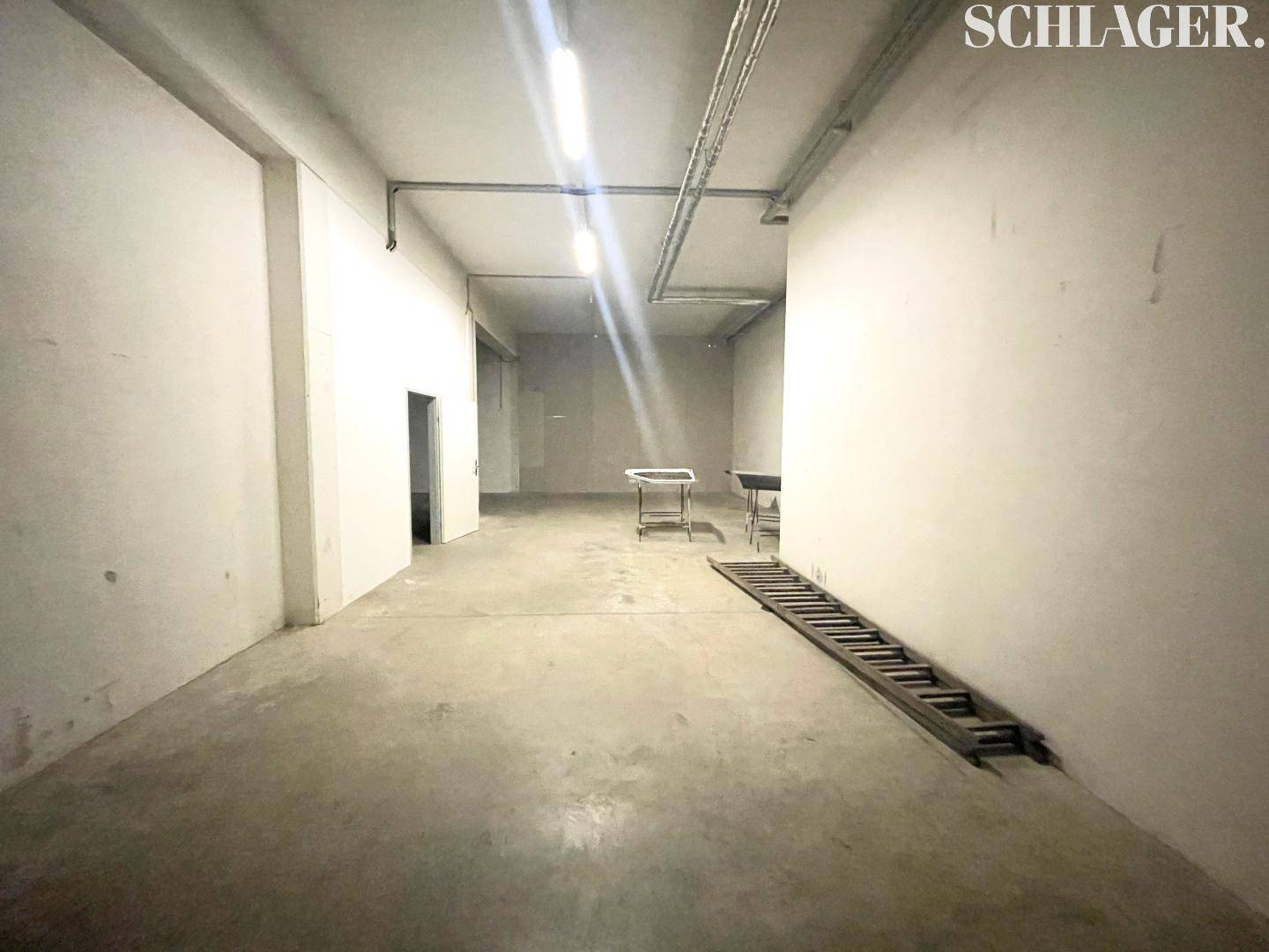 Großer, leerer Lagerraum mit Betonboden, hohen Decken und sichtbaren Installationen, bereit zur Nutzung.