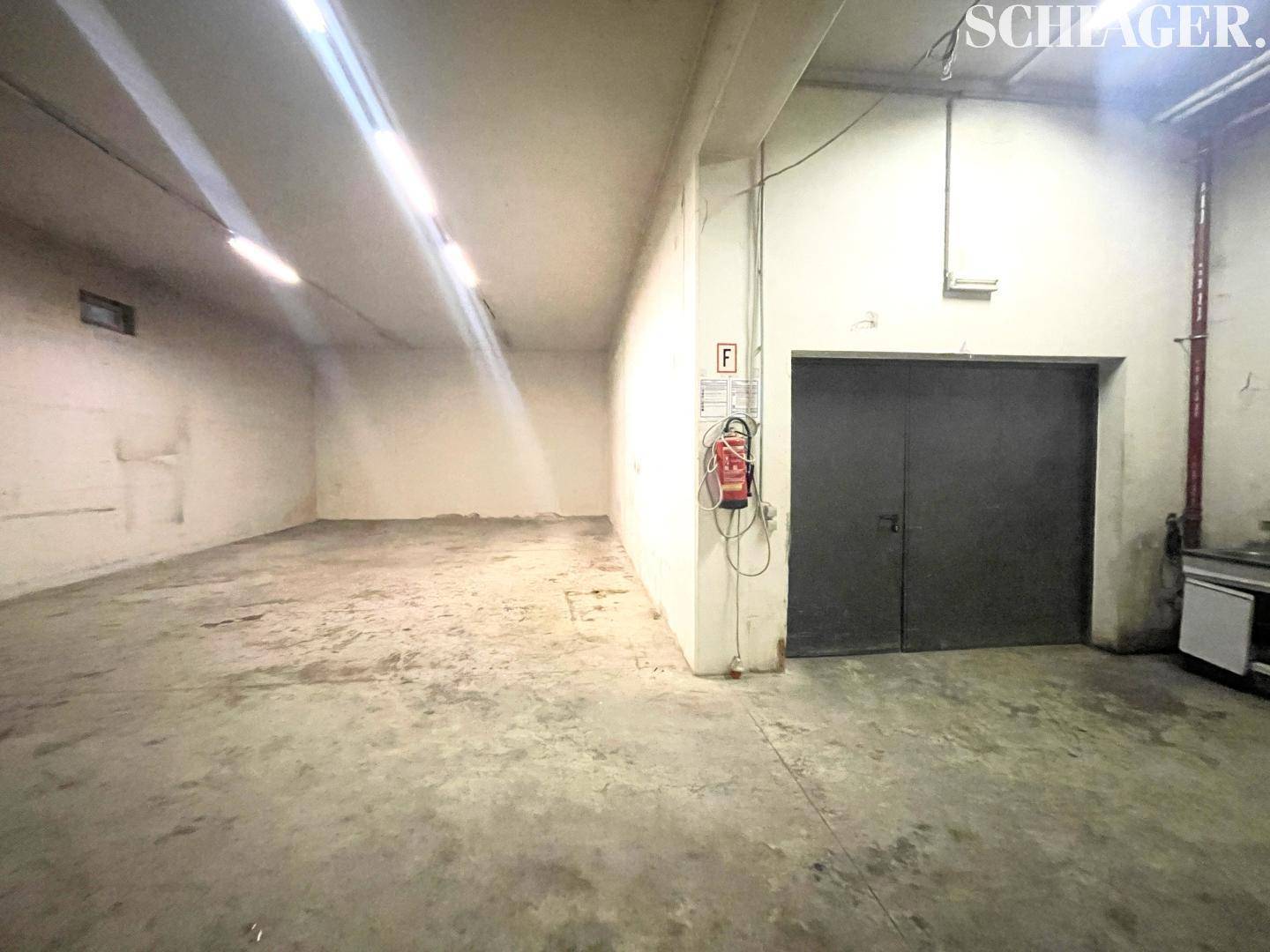 Geräumige Lagerhalle mit Betonboden, hohen Decken und großem Tor, ausgestattet mit Brandschutz.