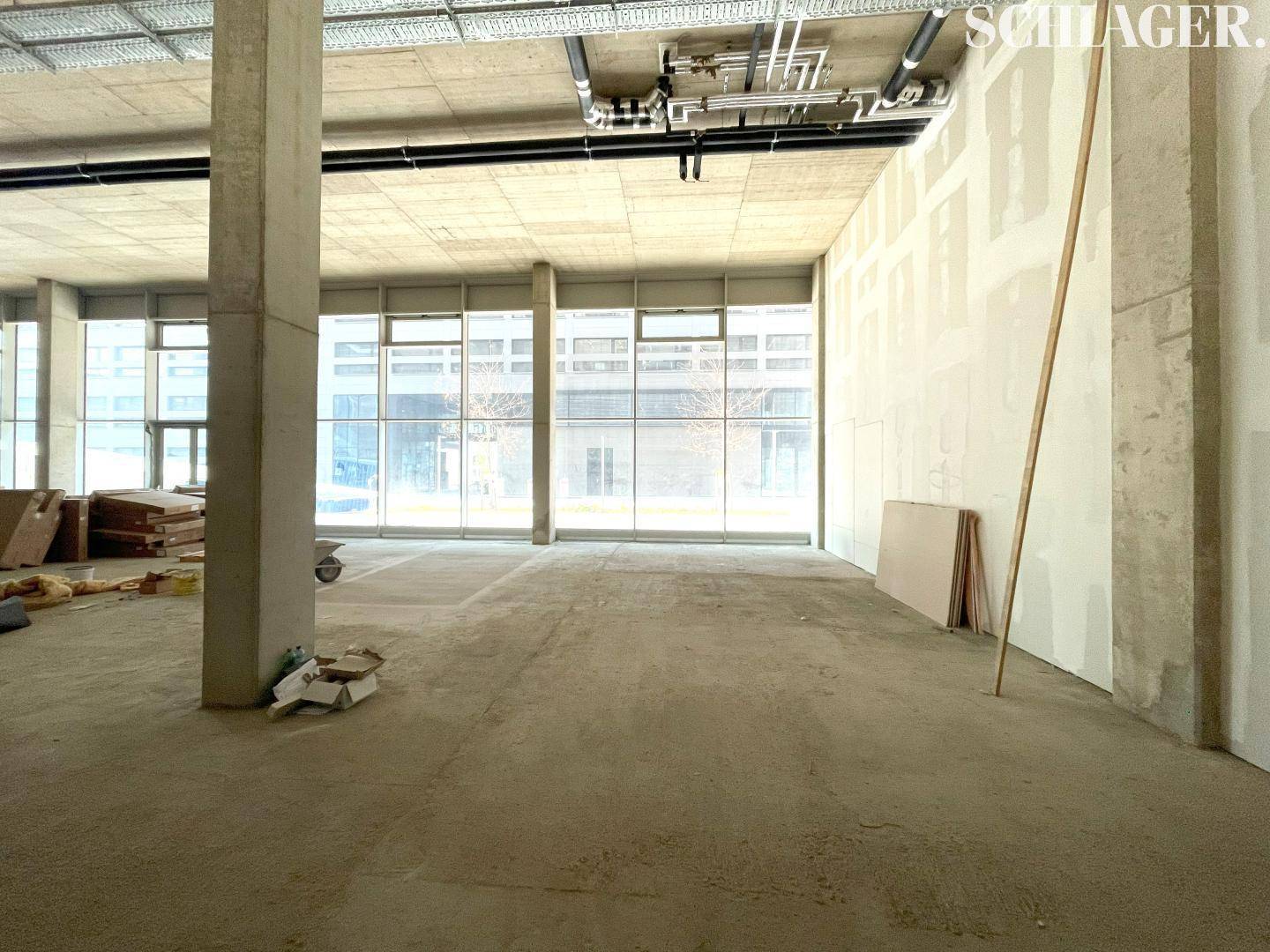 Unfertiger Gewerberaum mit hohen Decken, Betonpfeilern und großen Fensterfronten, bereit für den Ausbau.