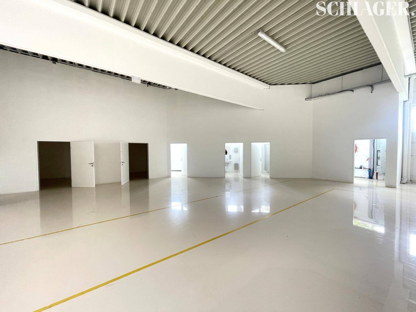 Geräumige Halle mit hohen Decken, glänzendem Boden und mehreren Zugangstüren im Hintergrund.