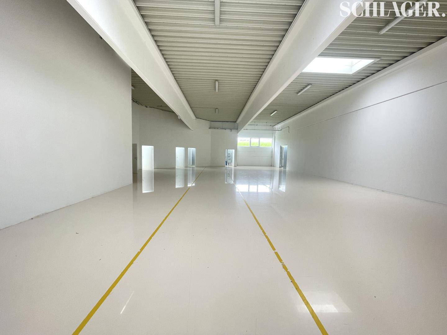 Lange, helle Lagerhalle mit hohen Decken, glänzendem Boden und gelben Markierungen auf dem Boden.