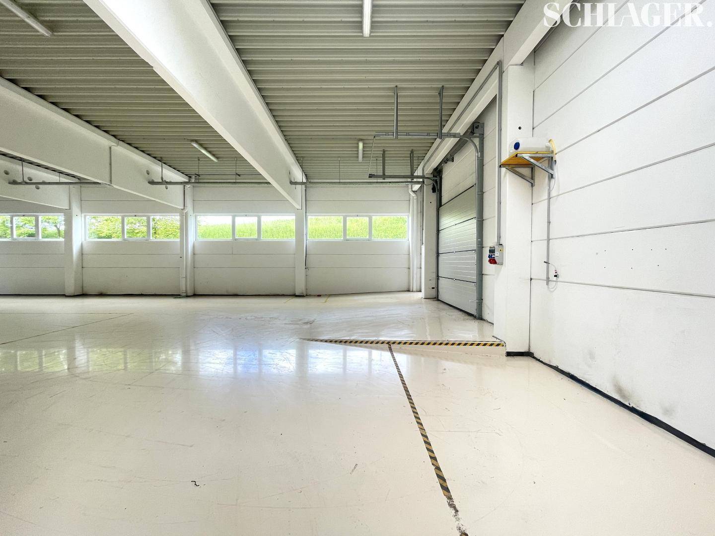 Geräumiger Industrieraum mit einem großen Rolltor und Fensterbändern, ideal für Anlieferung und Lagerung.