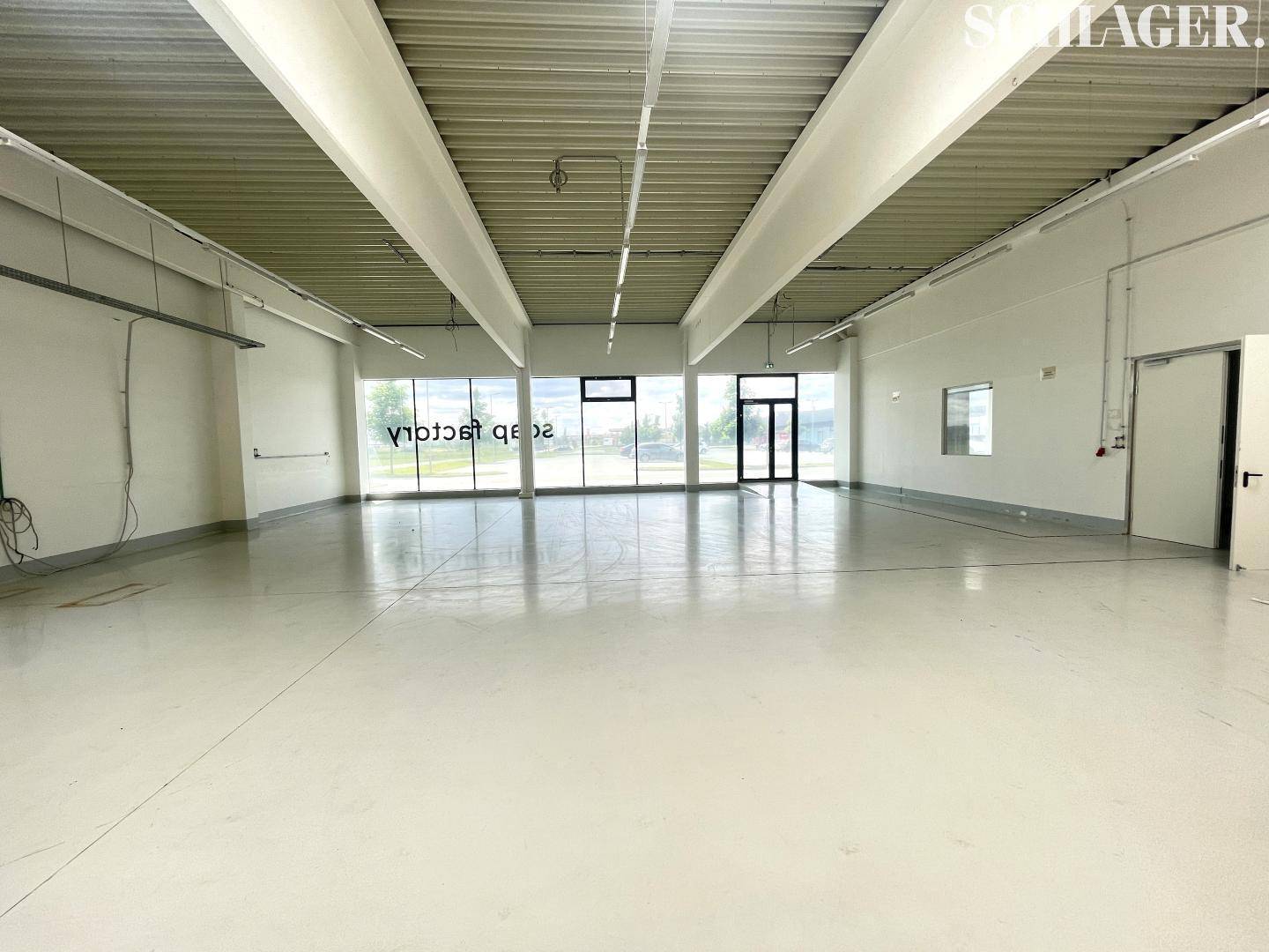 Heller, offener Gewerberaum mit großen Fensterfronten und glänzendem Boden, ideal für Einzelhandel oder Büro.