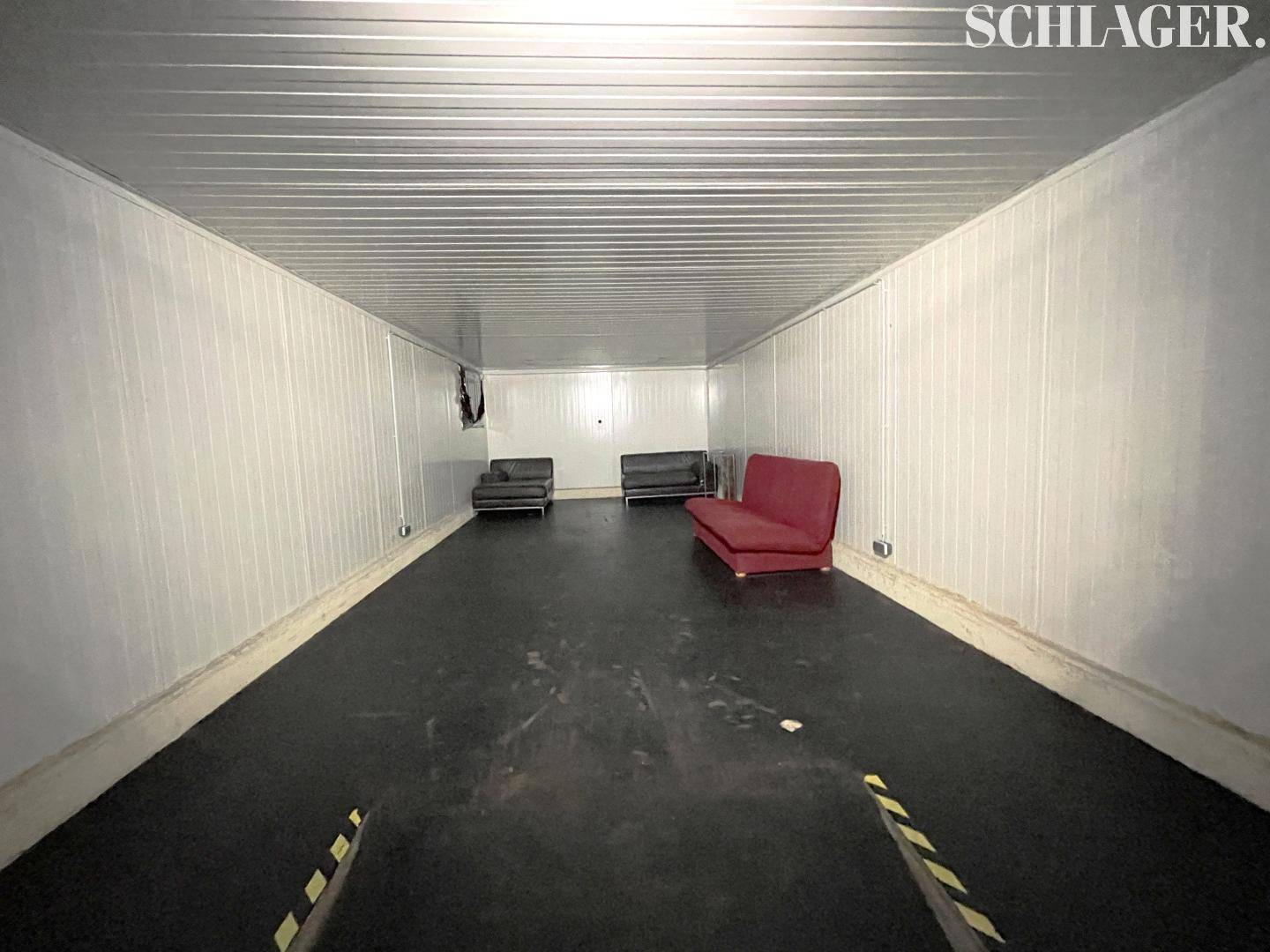 Länglicher Aufenthaltsraum mit dunklem Boden, weißen Wänden und mehreren Sofas.
