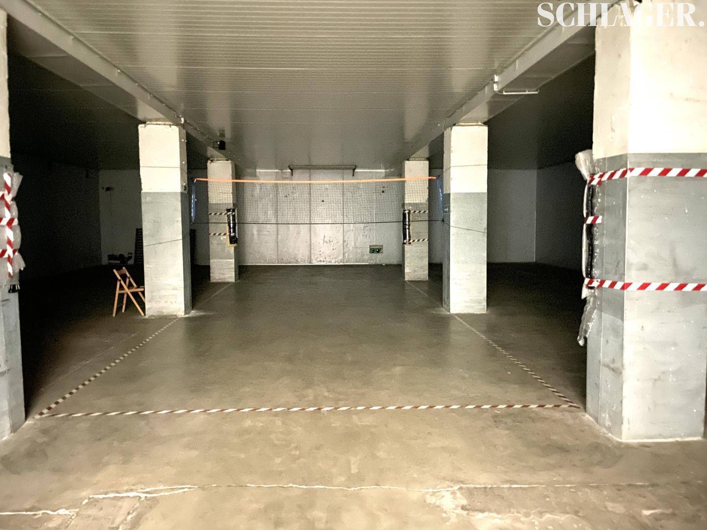 Großer, leerer Lagerraum mit Betonboden und tragenden Säulen, markiert mit Absperrband.