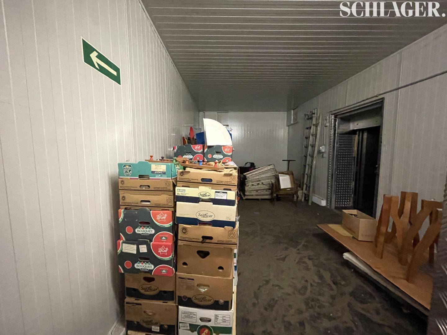 Lagerbereich oder Flur mit gestapelten Kartons, weißen Wänden und einem Lastenaufzug.
