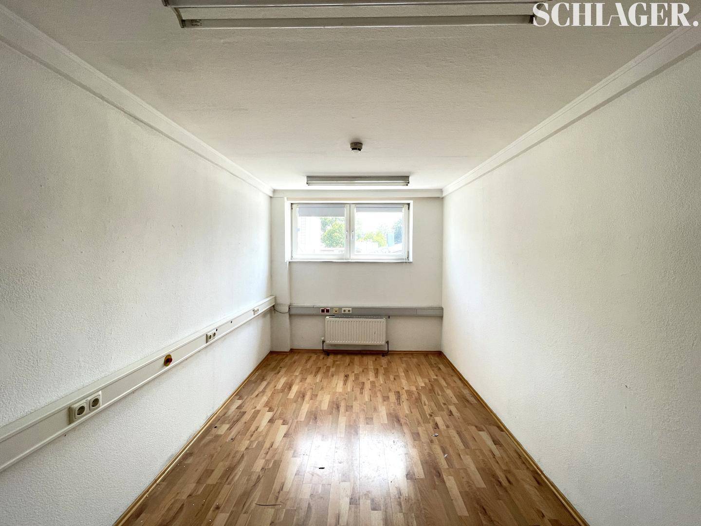 Kleinerer Büroraum mit einem Fenster, Laminatboden und weißen Wänden, ideal für Einzelbüro.
