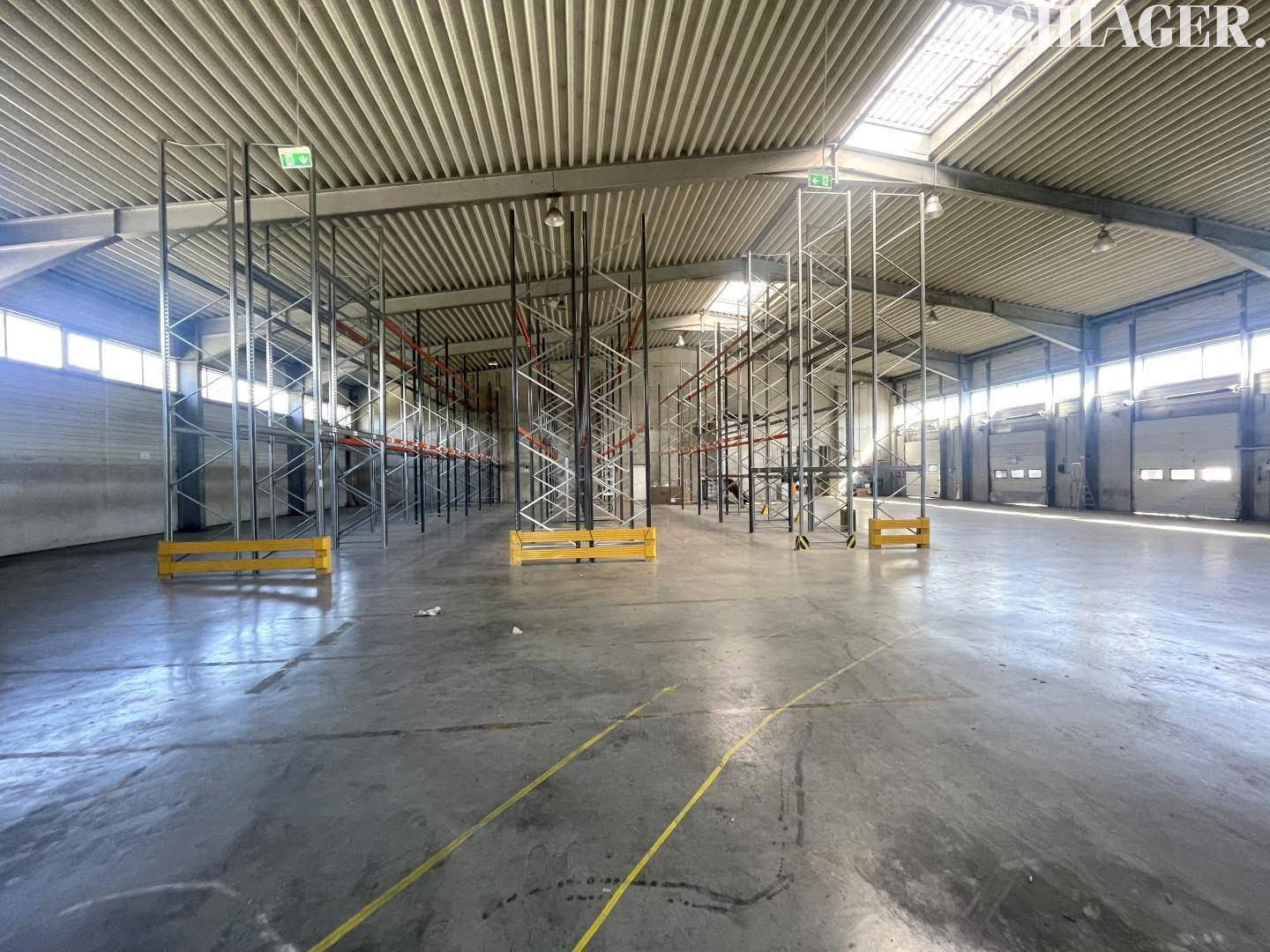 Große Lagerhalle mit Betonboden, hohen Decken und leeren Hochregalen, bereit zur Nutzung.