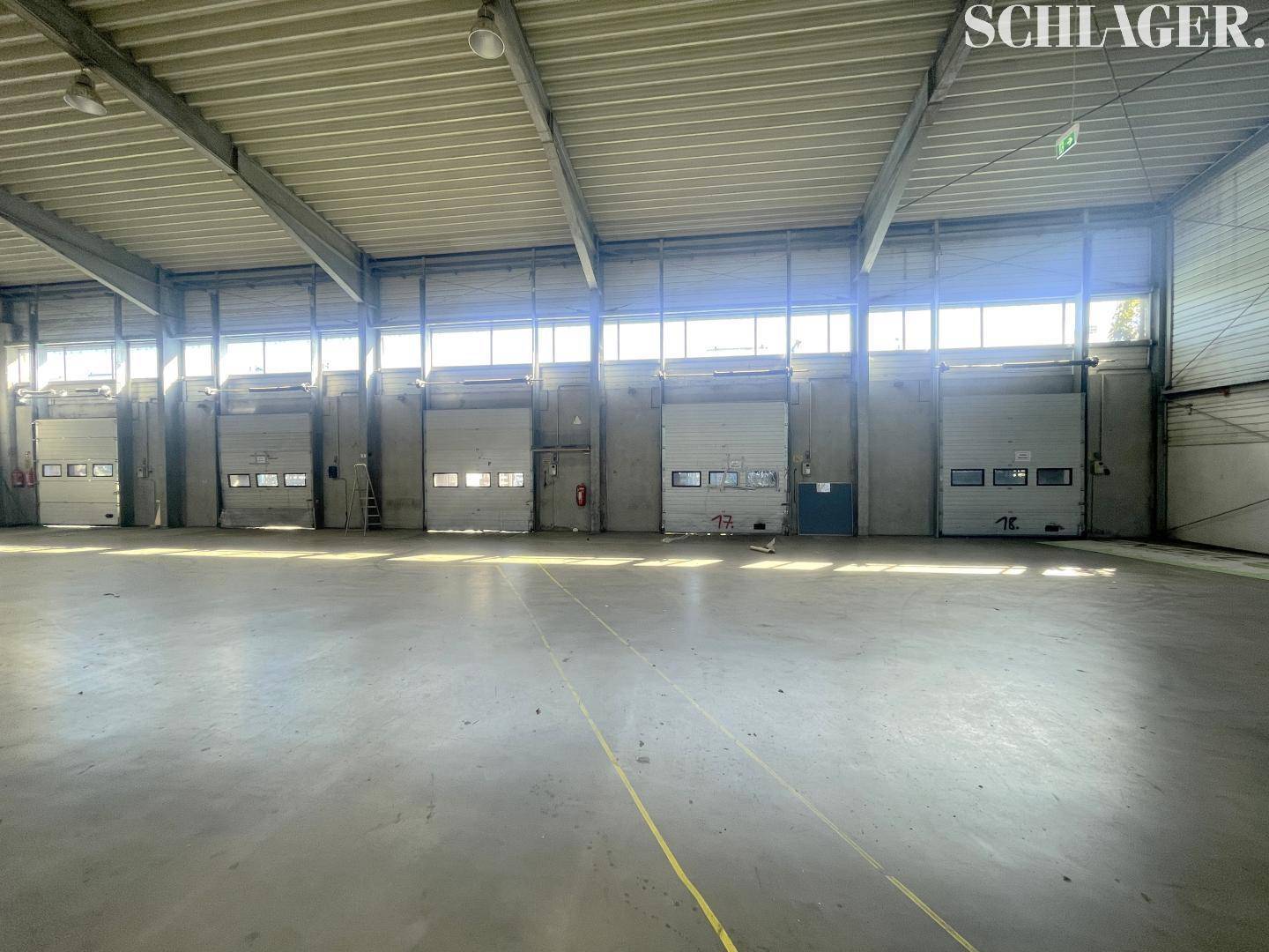 Großer Lagerraum mit Betonboden, hohen Decken und zahlreichen Rolltoren für effiziente Logistik.
