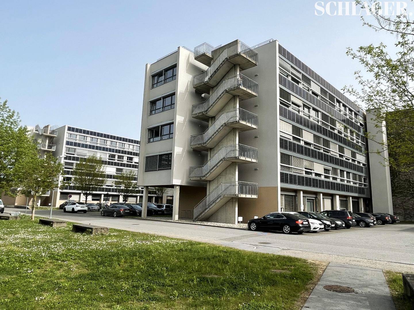 Modernes Bürogebäude mit markanter Außentreppe und zahlreichen Parkplätzen im Freien.