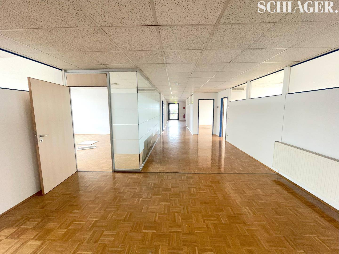 Langer Büroflur mit Parkettboden, Glaswänden und Türen zu einzelnen Büroräumen.