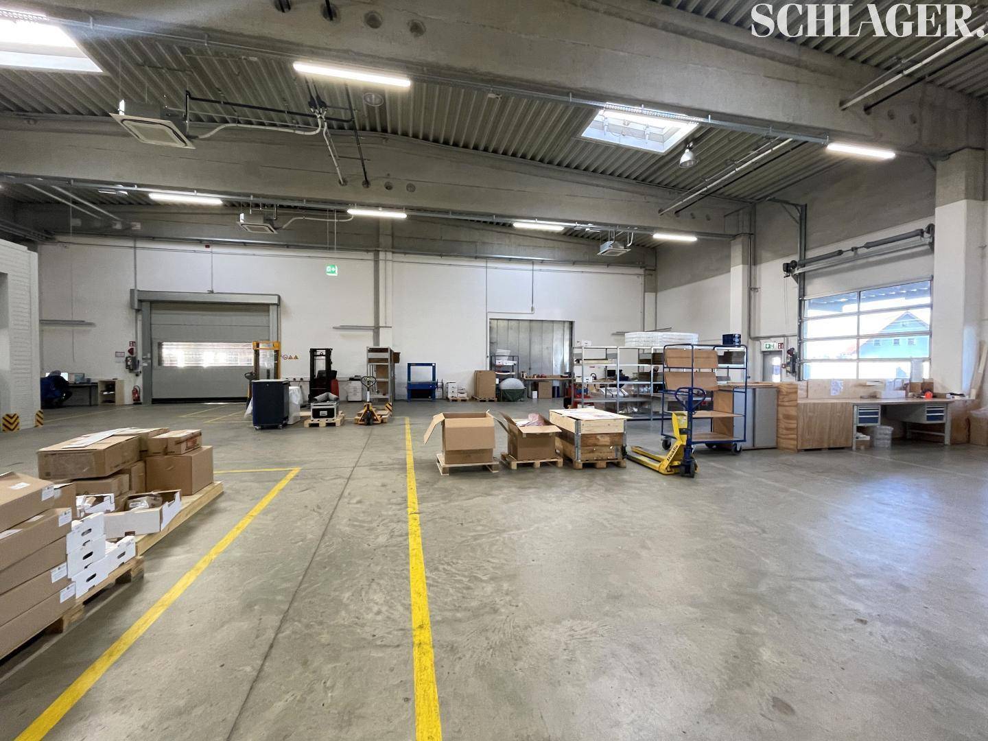Weitläufige Lagerhalle mit Betonboden, Rolltoren und natürlichem Lichteinfall durch Oberlichter.