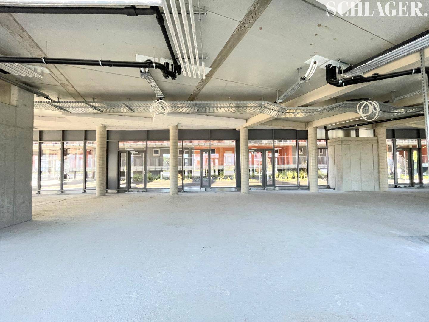 Geräumiger Gewerberaum mit Betonboden und großen Fenstern, bereit für den Innenausbau.