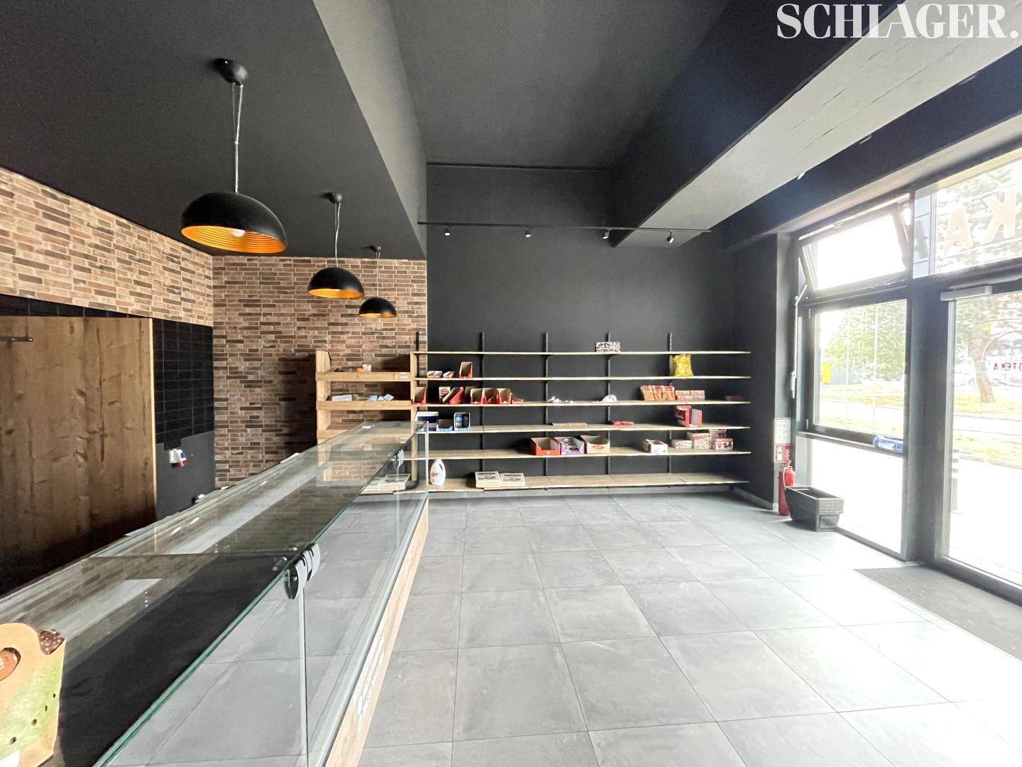 Ein moderner Ladenraum mit dunkler Decke, grauen Fliesen und einer Ziegelwand, ausgestattet mit Regalen und einer Theke.