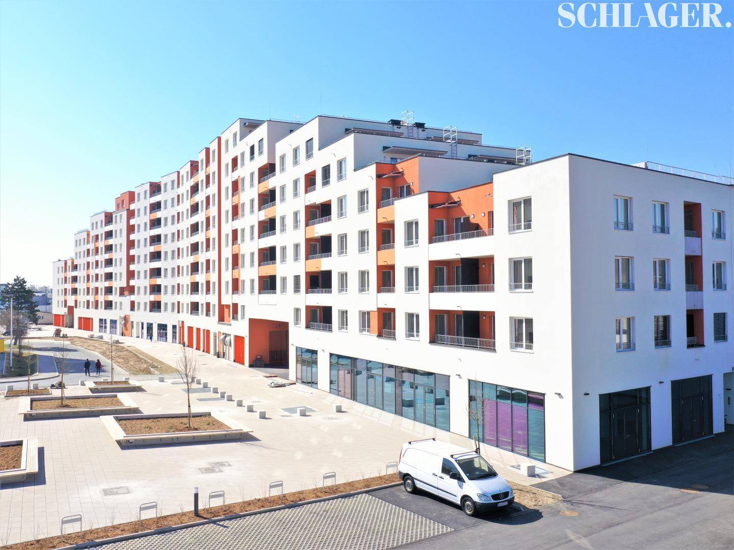 Eine Nahaufnahme des modernen Wohnkomplexes mit Geschäften im Erdgeschoss und einer gepflasterten Fläche davor.