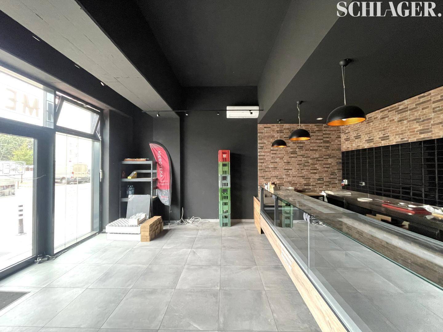 Innenansicht eines Ladenlokals mit großen Fenstern, dunkler Decke und einer Ziegelwand, ideal für gewerbliche Nutzung.