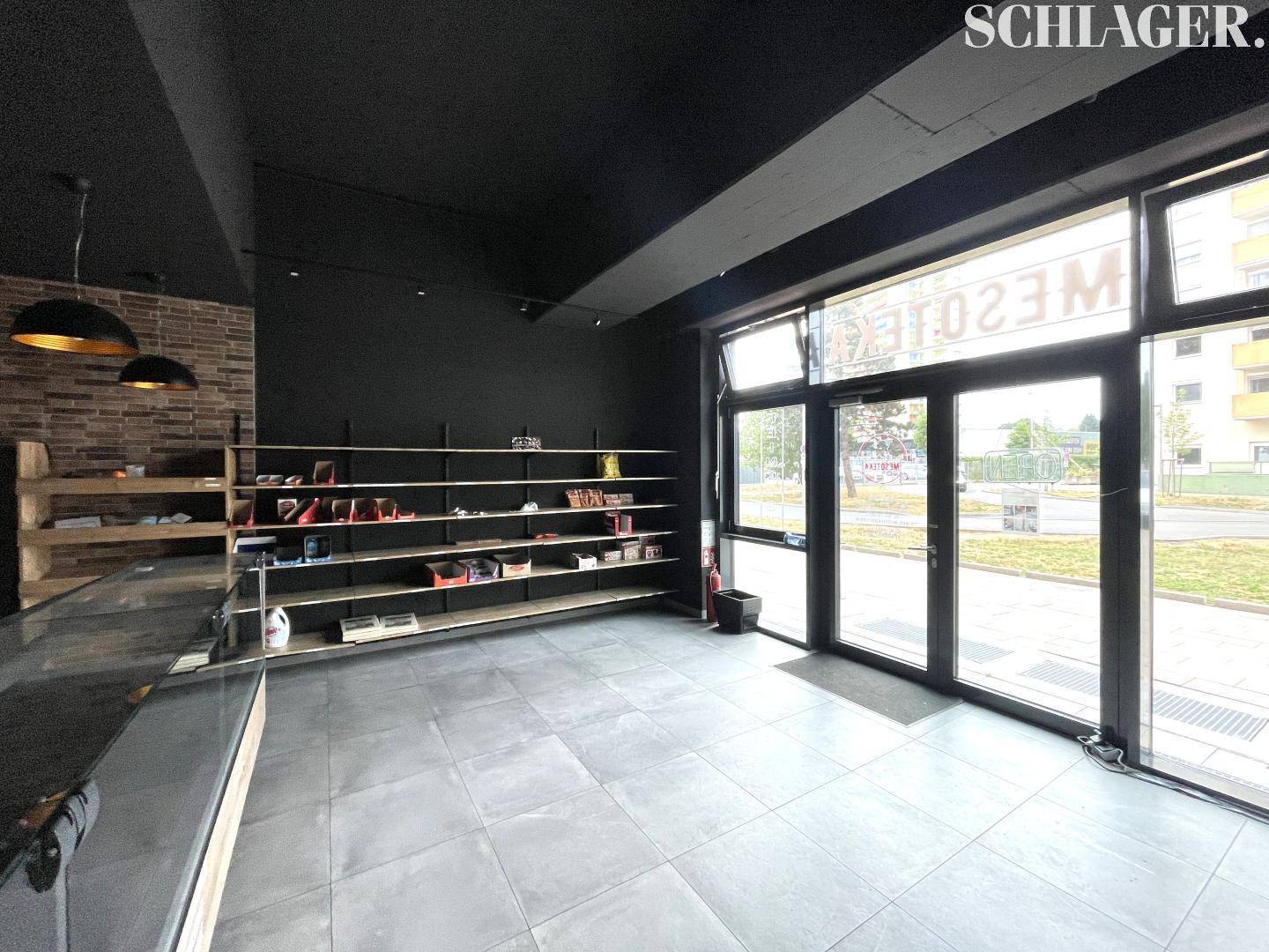 Geräumiger Ladenbereich mit großen Schaufenstern, dunkler Decke und Regalen, die vielseitige Nutzungsmöglichkeiten bieten.