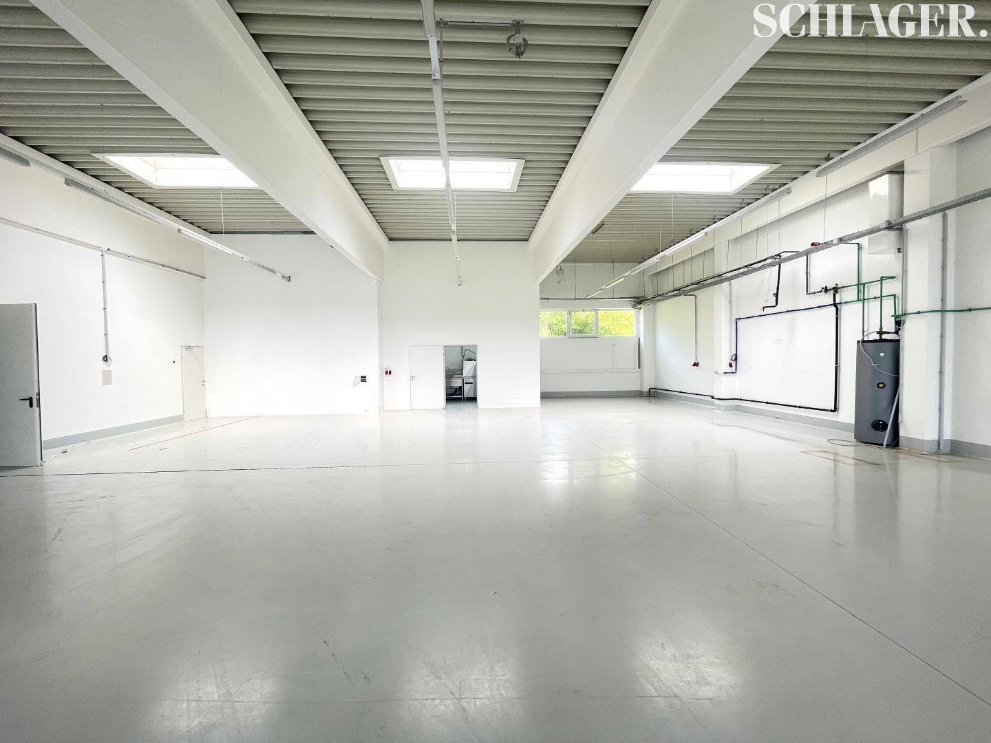 Innenansicht der Gewerbefläche mit Oberlichtern, hohen Decken und sichtbaren Installationen an den Wänden.